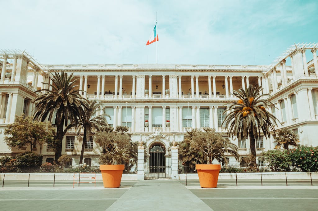Elegant facade of the Prefecture Palace in Nice with palm trees and French flag.